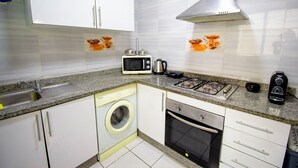 Een functionele keuken met wasmachine, magnetron, oven en gasfornuis.