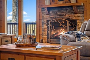 Ein gemütliches Wohnzimmer mit Kamin, einem Holztisch mit einer Karaffe und Gläsern für Whiskey und einem bequemen Sofa.
