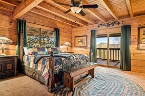 A wooden cabin bedroom with a bed, a bench, a table, and a view of the outdoors. - Cabin w/ 2 Hot Tubs · Theater · Game Room (Sevierville)