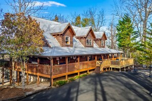A cabin with a metal roof, wooden deck, and a covered porch. - Cabin w/ 2 Hot Tubs · Theater · Game Room (Sevierville)