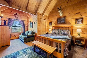 A log cabin bedroom with a bed, a bench, a chair, and a window. - Cabin w/ 2 Hot Tubs · Theater · Game Room (Sevierville)