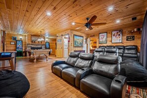 A cozy room with a wooden ceiling, a leather sofa, a pool table, and a gaming area. - Cabin w/ 2 Hot Tubs · Theater · Game Room (Sevierville)
