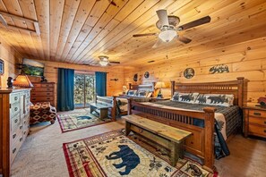 Ein Urlaubsdomizil mit Holzbalkendecke, einem Bett mit tierischen Motiven auf der Bettwäsche, einer Bank, einem Schminktisch und einem Deckenventilator.