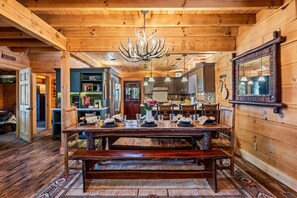 A wooden interior with a dining table set for four, a chandelier, and a mirror on the wall. - Cabin w/ 2 Hot Tubs · Theater · Game Room (Sevierville)