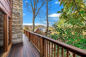 Une terrasse en bois avec un mur en pierre, offrant une vue sur un paysage montagneux, avec des arbres et un ciel dégagé.