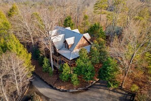 A large, multi-story house with a complex roof structure surrounded by dense forest. - Cabin w/ 2 Hot Tubs · Theater · Game Room (Sevierville)