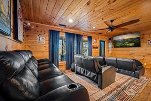 L’intérieur d’un chalet en rondins, avec des canapés en cuir, un ventilateur de plafond et une vue magnifique par les fenêtres.