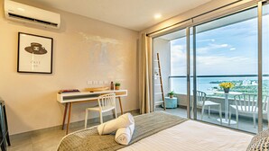 Una habitación de hotel con cama, escritorio, silla, balcón con vistas al mar y un cuadro en la pared.