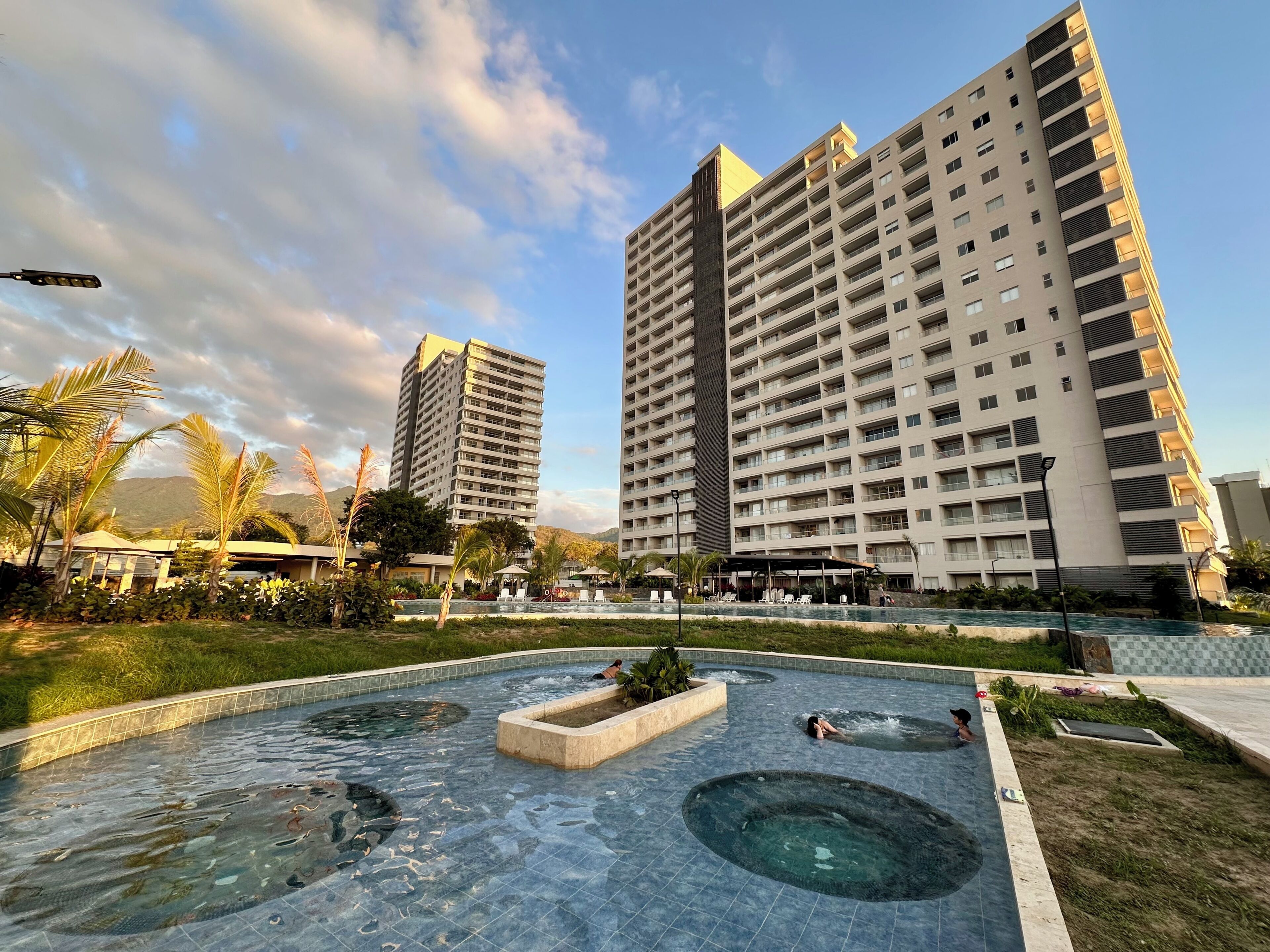 Un hotel moderno con zona de piscina en la azotea, que incluye un jacuzzi y una fuente.