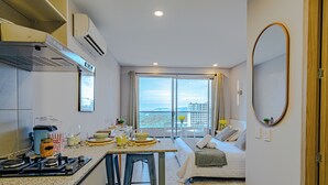 Habitación de hotel compacta con kitchenette, zona de comedor, cama y un amplio ventanal con vistas a la ciudad.