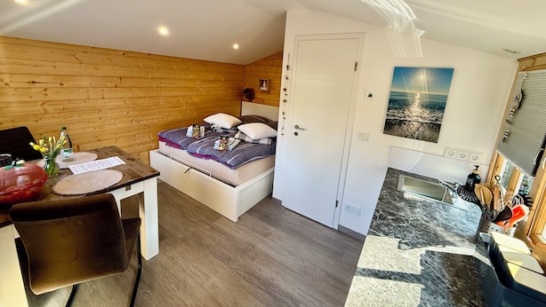 Ein Zimmer mit einem Bett, einem Schreibtisch mit einem Laptop, einem Esstisch und einer Küchenzeile mit Herd und Kochutensilien.
