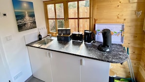 Eine Küche mit Marmorarbeitsplatte, Holzschränken, einem Spülbecken, einer Kaffeemaschine und einem Fenster mit Blick auf Bäume.