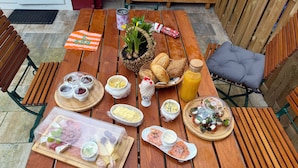 Ein Holztisch mit verschiedenen Speisen, darunter Brot, Käse und Gewürzen, gedeckt für eine Mahlzeit.
