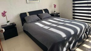 A bedroom with a bed, nightstands, a framed picture, and a window with blinds. - 1415 2-bedroom apartment in serene Manzanillo with AC for comfort (Manzanillo)