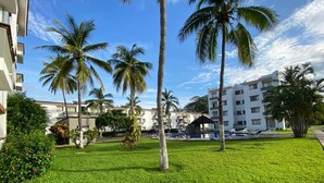 A hotel courtyard with palm trees, a pool, and a building with balconies. - 1415 2-bedroom apartment in serene Manzanillo with AC for comfort (Manzanillo)