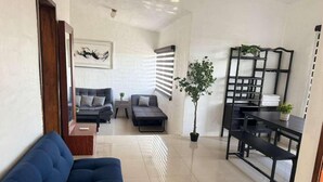 A living room with a blue sofa, a dining table with benches, a potted plant, and a wall-mounted shelf. - 1415 2-bedroom apartment in serene Manzanillo with AC for comfort (Manzanillo)