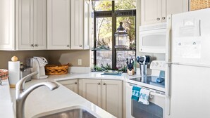Una cocina con armarios blancos, un fregadero, un microondas y una ventana con vistas a árboles.
