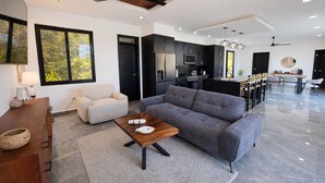 Un salon moderne avec un canapé gris, une table basse en bois et un coin repas comprenant des chaises, avec une cuisine en arrière-plan.