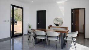 Un espace repas moderne avec une table en bois, quatre chaises grises, un ventilateur de plafond et un grand miroir au mur.