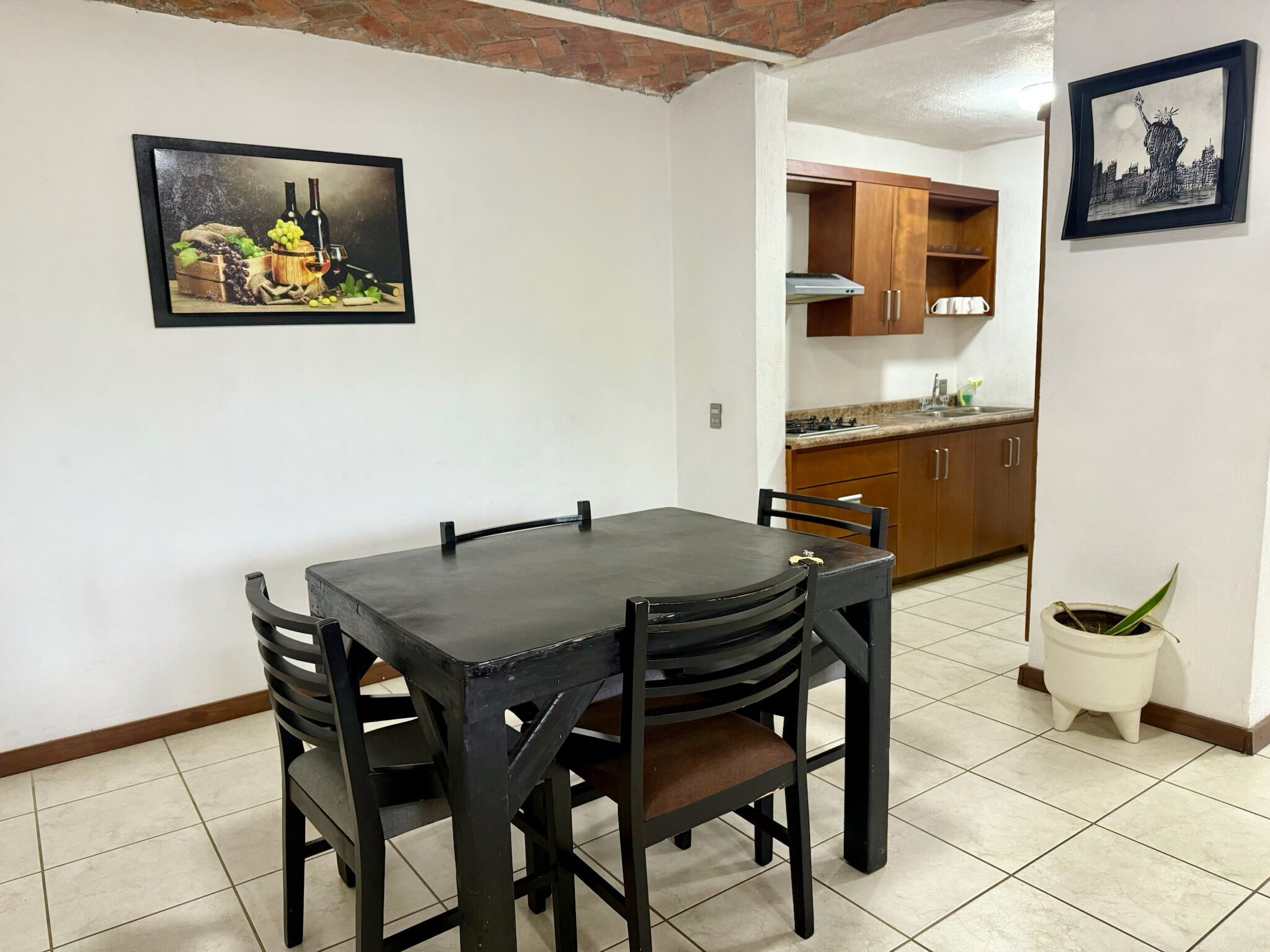 Un comedor con una mesa y sillas, una cocina al fondo y un cuadro en la pared.