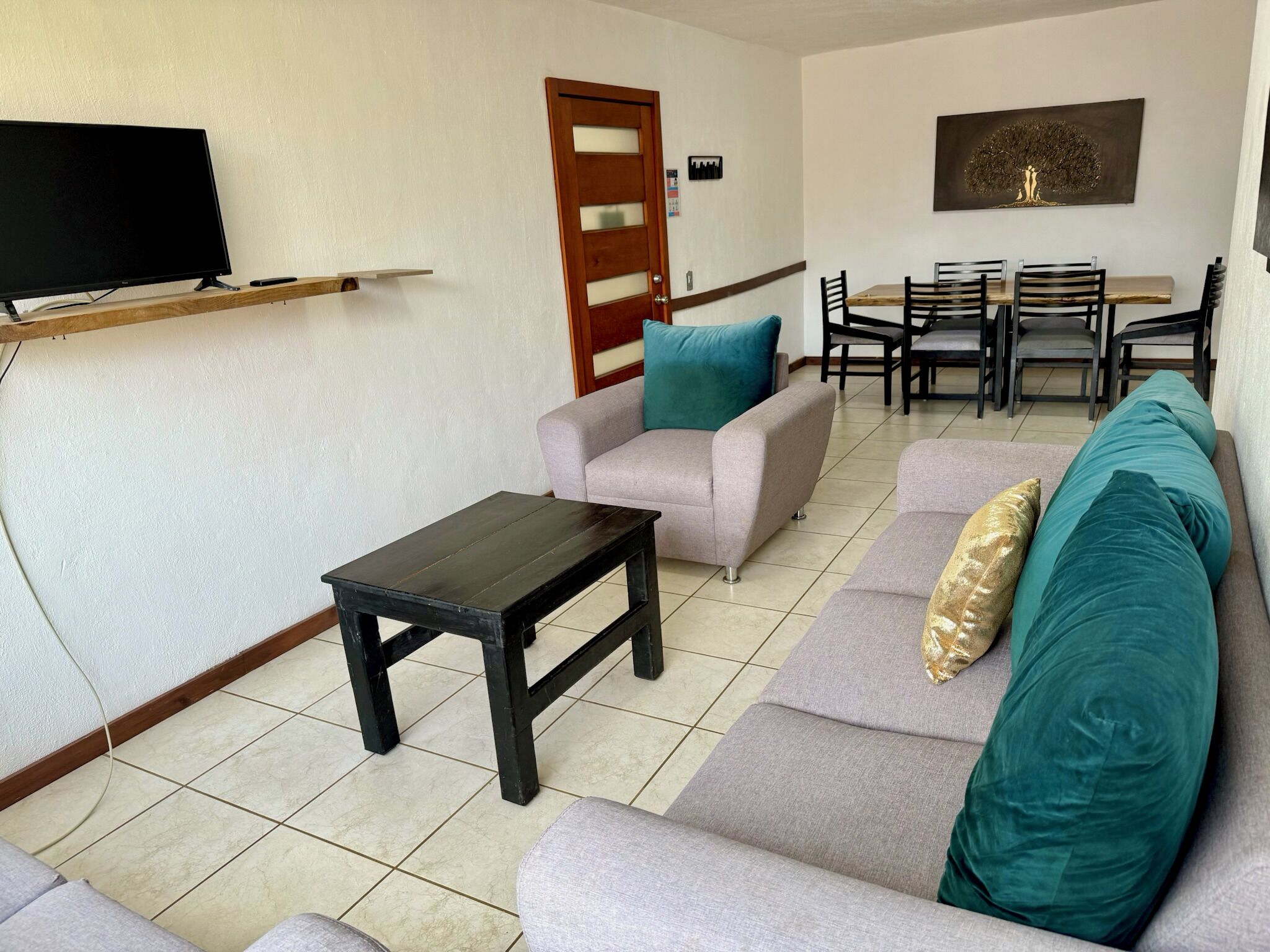 Una sala de estar con sofá, sillón, mesa de centro, televisor y comedor.