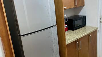 Eine Küche mit Kühlschrank, Mikrowelle, Holzschränken und Fliesenboden.