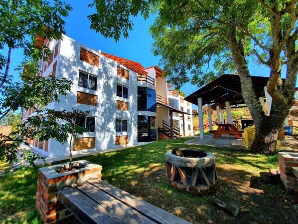 A courtyard with a building, a tree, a fire pit, and a wooden bench. - Herradura VIP Inn (Mazamitla)