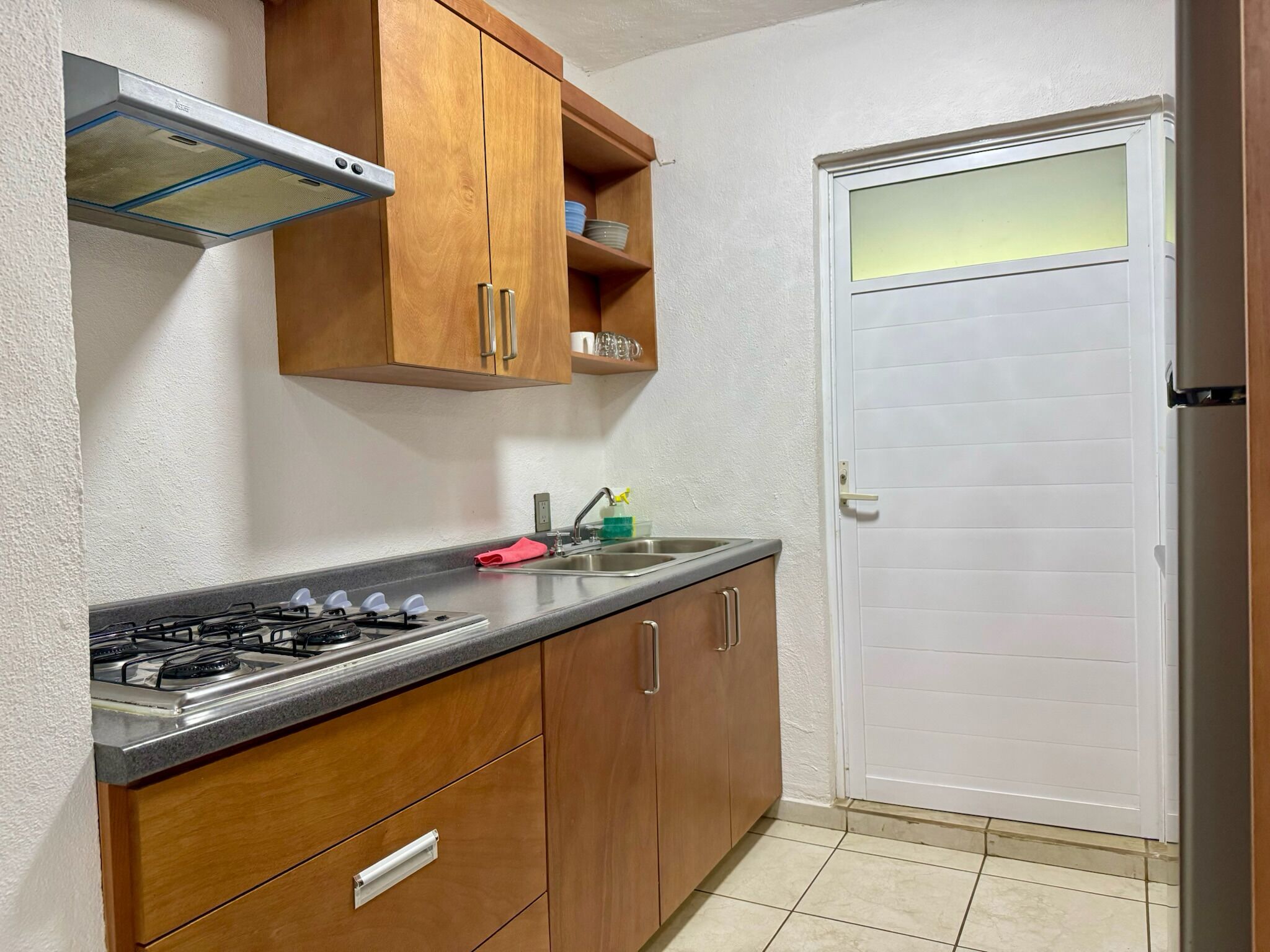 A kitchen with wooden cabinets, a gas stove, a stainless steel sink, and a white door.