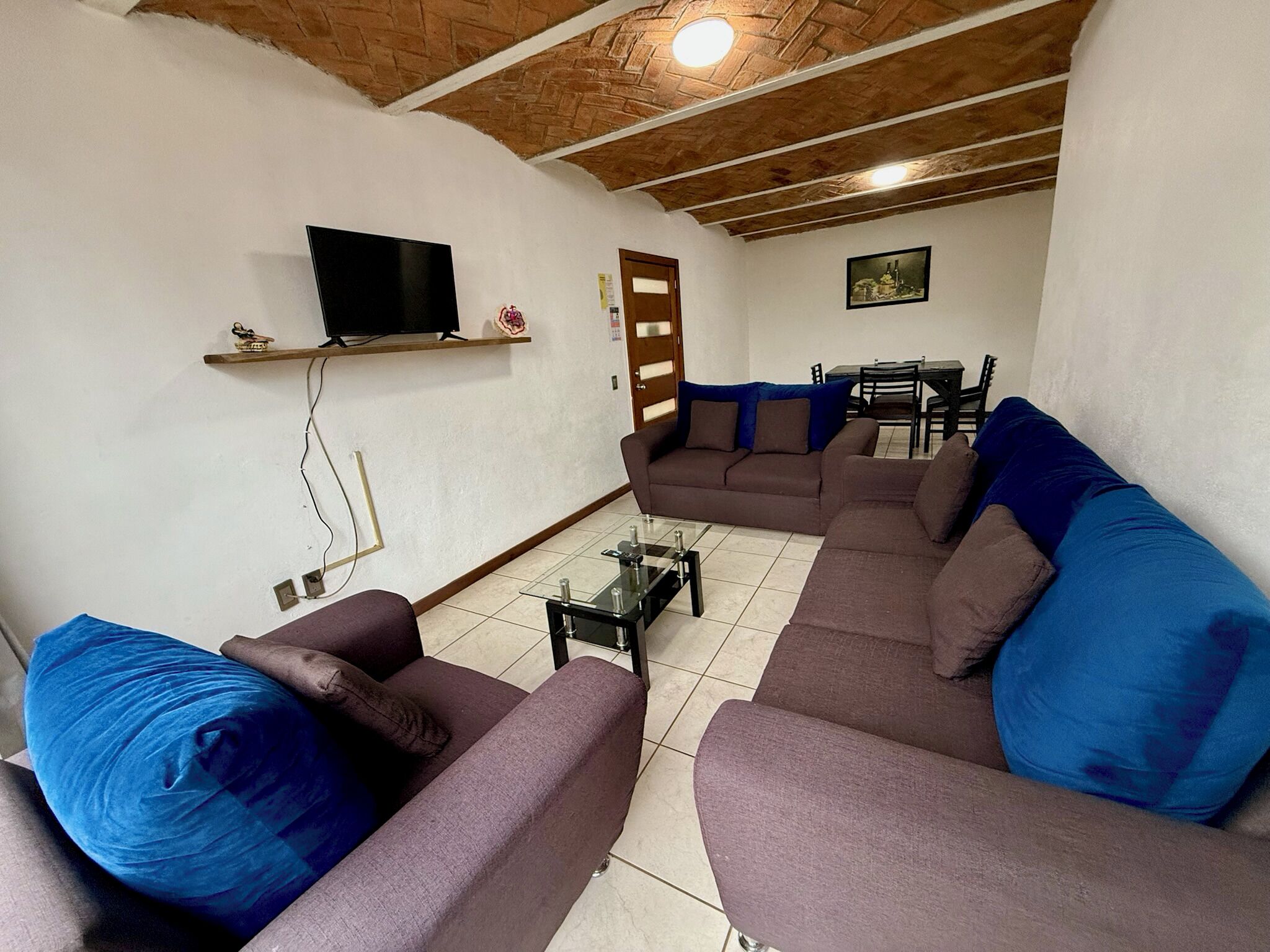 Una sala de estar con televisión, sofás, una mesa de centro y un comedor al fondo.