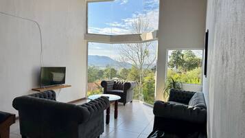 Una sala de estar moderna con televisor, dos sofás y vistas a montañas y árboles.