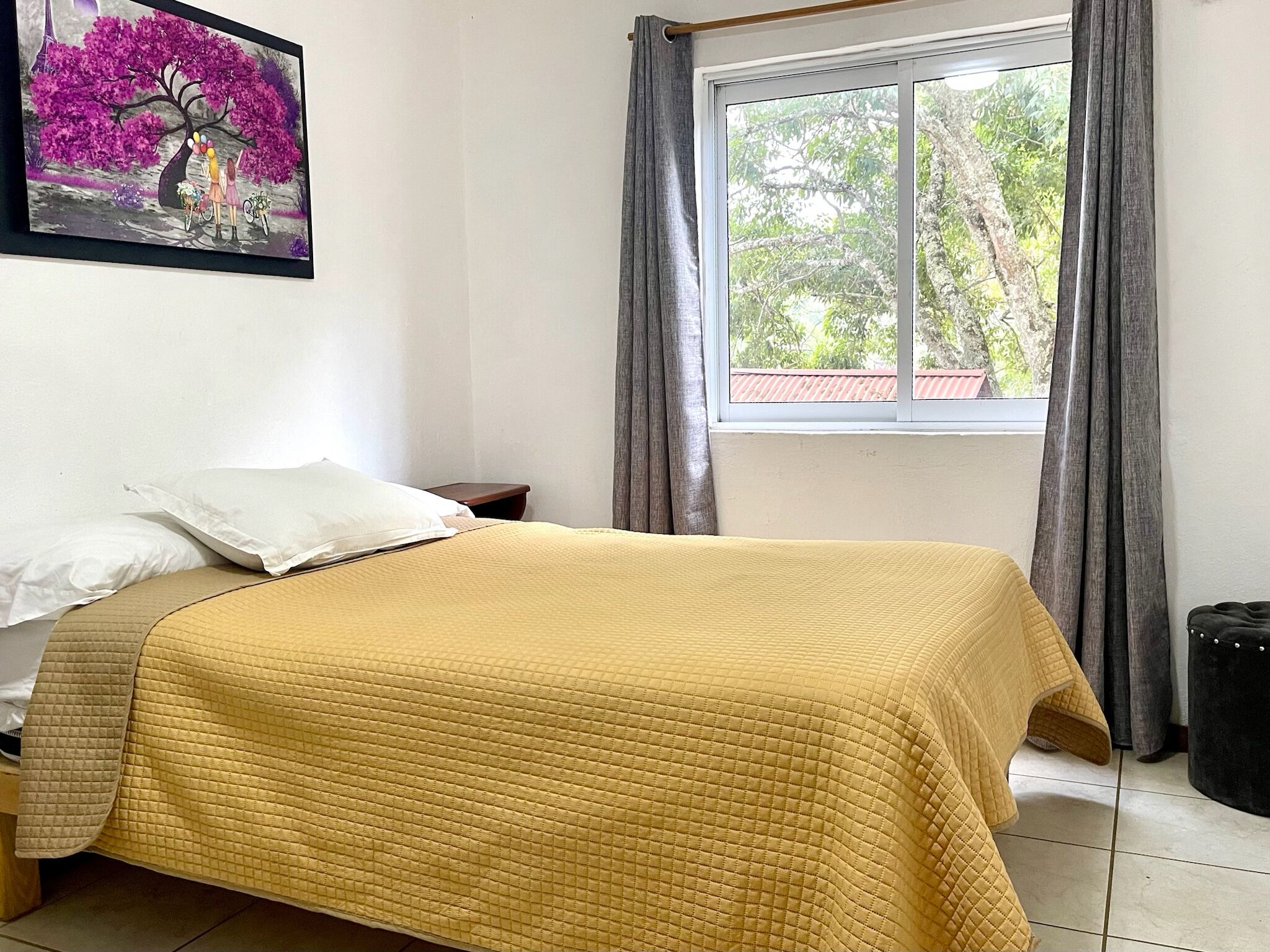 Una cama con cubrecolcha amarillo acolchado, almohada blanca y mesita de noche con lámpara.