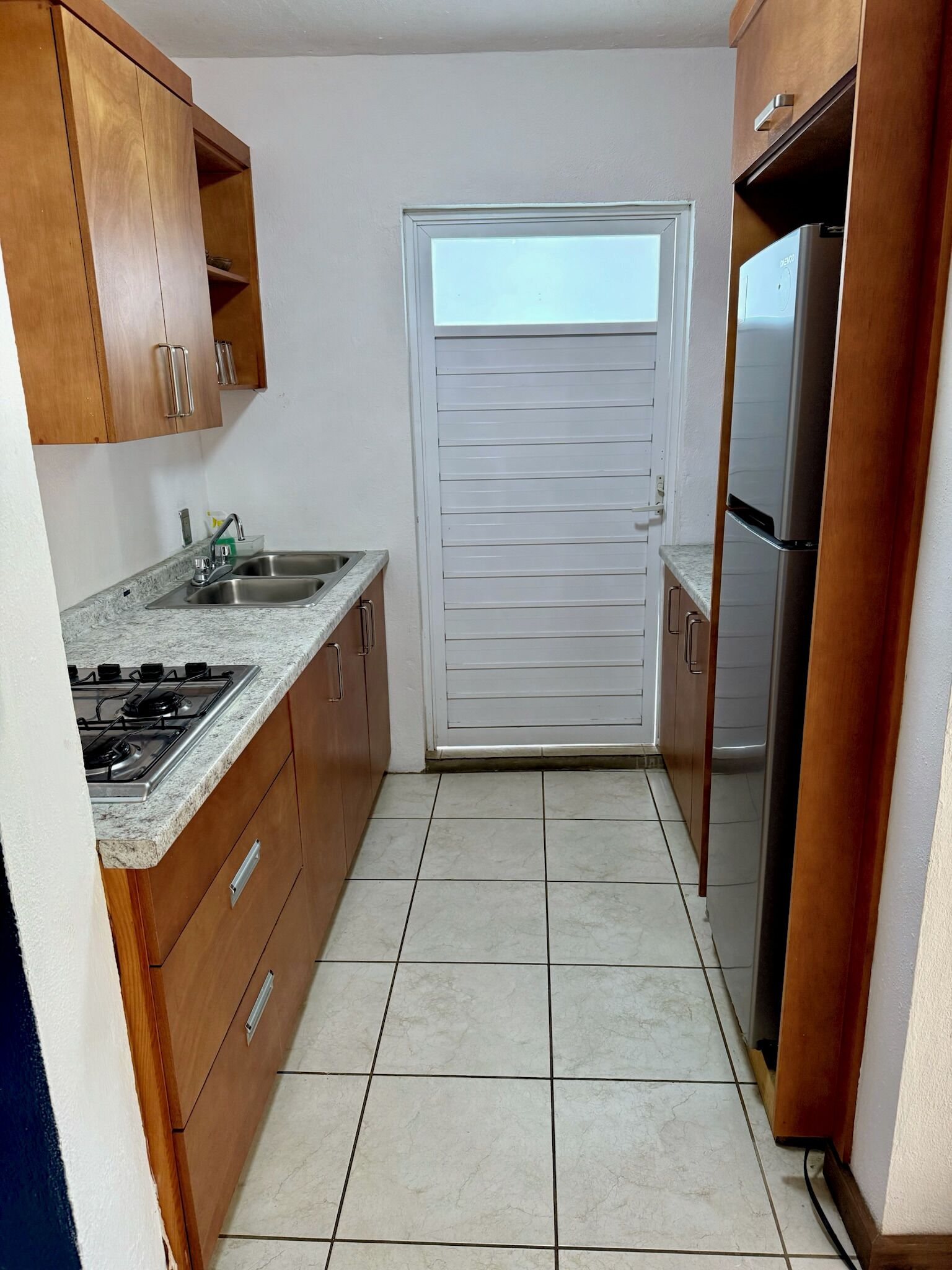 A compact kitchen with a gas stove, stainless steel sink, wooden cabinets, and a built-in refrigerator.