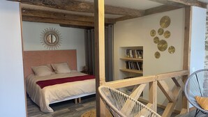 Een slaapkamer met een houten plafond, een bed met een rode deken, een wand met decoratieve borden en een rieten stoel.