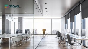 Un espace de bureau moderne doté de cloisons en verre, de nombreux postes de travail et de grandes fenêtres offrant une vue sur la ville.