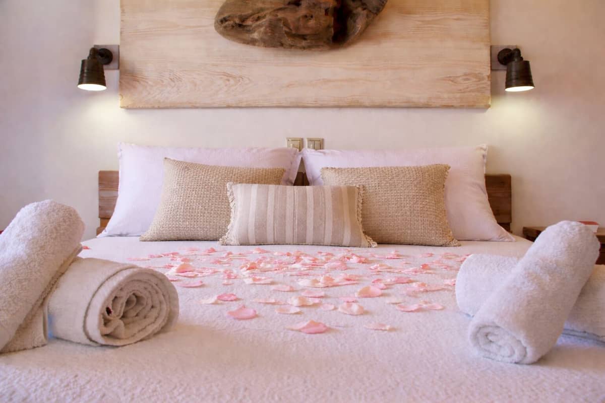 A hotel room with a bed, pillows, a wooden headboard, and wall-mounted lights.