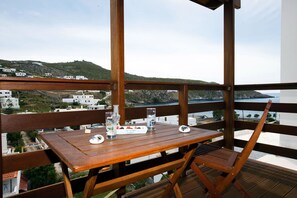 A wooden table and chair on a balcony with a view of a coastal landscape. - Mistral Patmos (Patmos)
