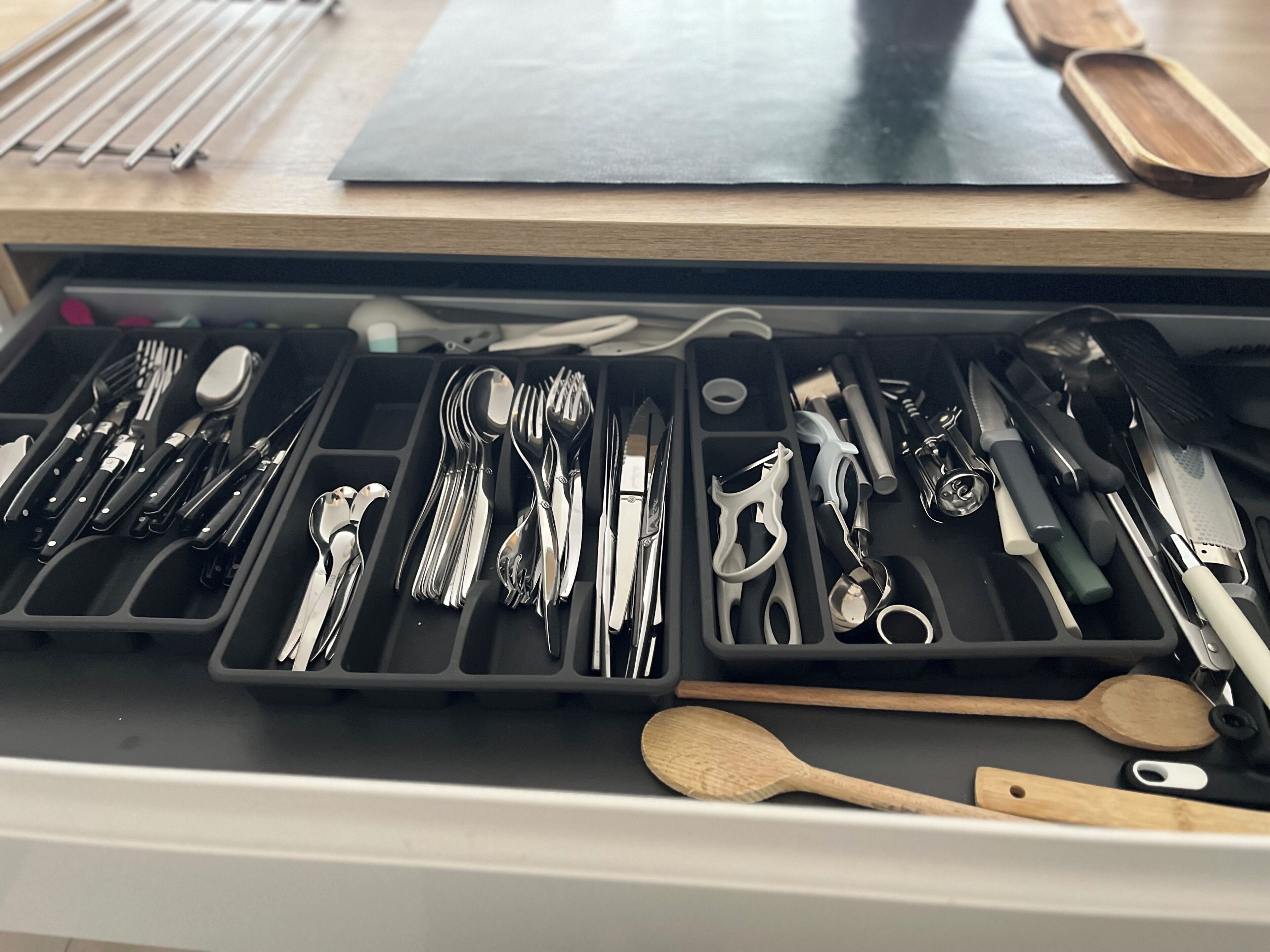A drawer with various kitchen utensils and tools, including knives, spoons, and a wooden spoon.