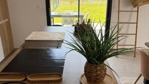 A room with a wooden table, a woven basket, a potted plant, and a view of a garden through a glass door. - La Lézardière House with swimming pool in Ruoms, close to nature and rivers (Ruoms)