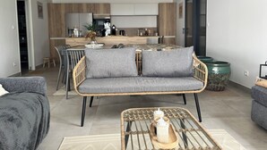 A modern living room with a grey sofa, wicker furniture, and a coffee table with decorative items. - La Lézardière House with swimming pool in Ruoms, close to nature and rivers (Ruoms)