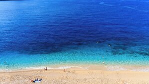 Een strand met helderblauw water, een zandstrand en een klein eiland in de verte.