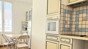 A kitchen with white cabinets, a microwave, and a stove. There is a dining table with chairs. - Cosy T2 in downtown Le Mans, 15 minutes from the 24h circuit (Le Mans)