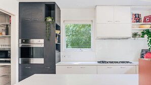 Una cocina moderna con horno empotrado, ventana con vistas al verdor, armarios blancos y estufa a gas.