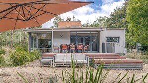 Una casa moderna con un patio, mobiliario exterior y un paraguas grande.