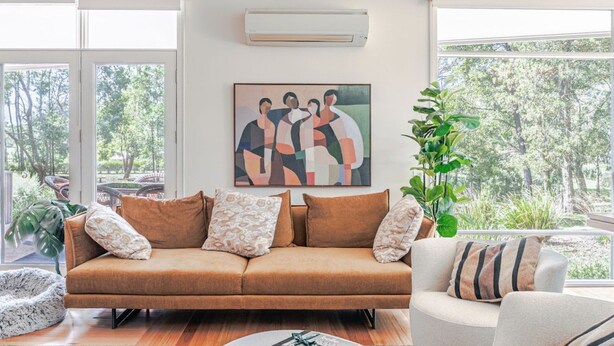Ein modernes Wohnzimmer mit einer Couch, einem Gemälde und Blick auf Bäume.