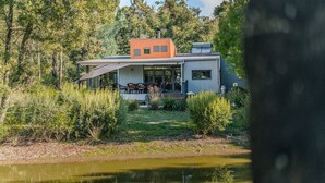 Una casa moderna con una terraza amplia, rodeada de abundante vegetación y un estanque.