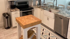 Una cocina moderna con armarios blancos, un lavavajillas de acero inoxidable, una mesa de madera y un piso con diseño.