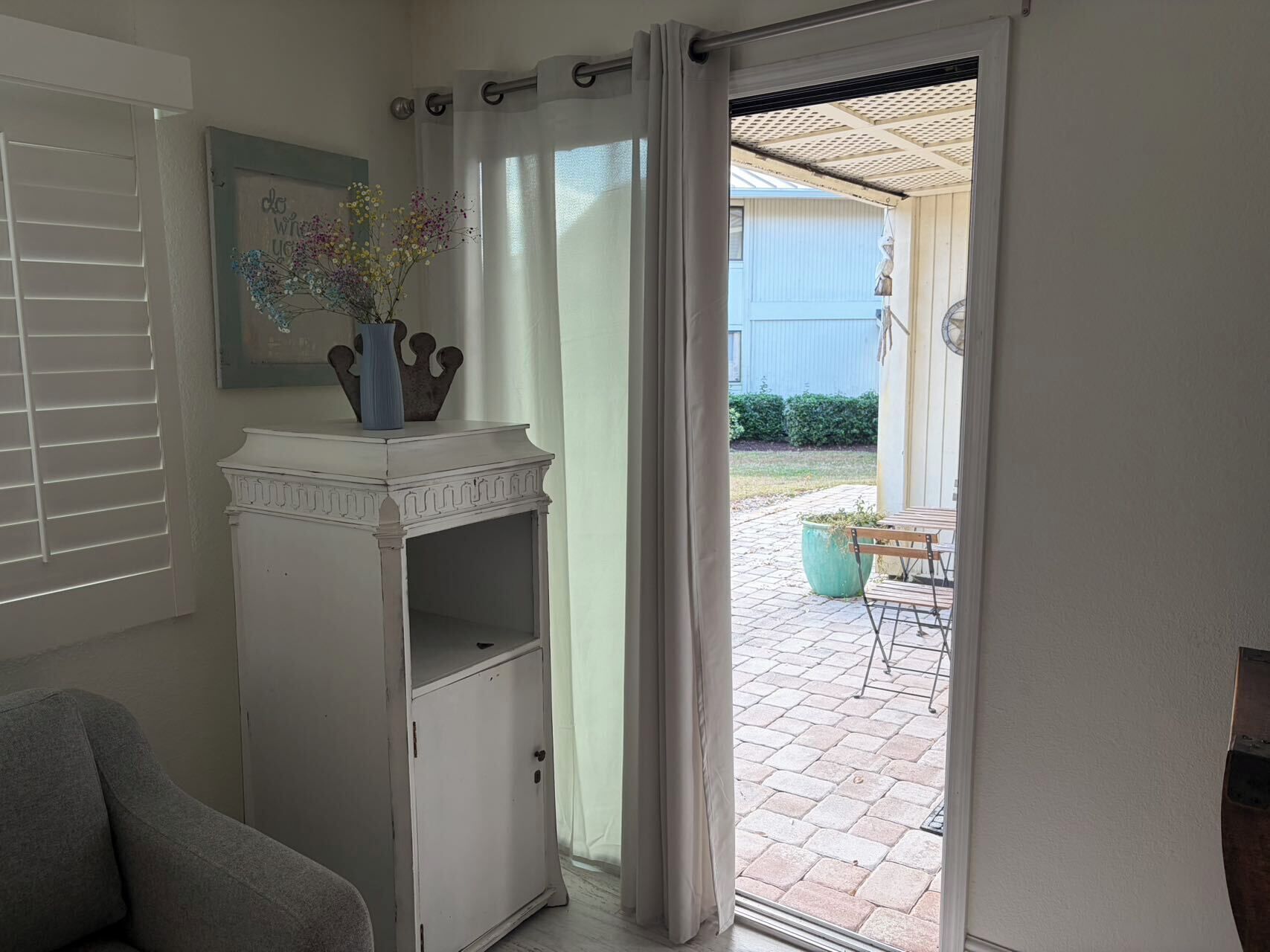Una habitación con un armario blanco, una silla, una puerta que da a un área exterior con un banco y una planta en maceta.