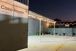 Una entrada con portón, un letrero que dice 'Casa Rayón' y un espacio al aire libre techado con guirnaldas de luces.