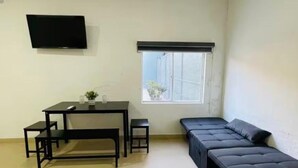 Ein Zimmer mit einem Bett, einem Schreibtisch, einem Stuhl, einem kleinen Tisch, einem Fernseher und einem Fenster.