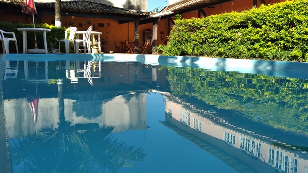 Ein klares Schwimmbecken mit Spiegelbild der umliegenden Architektur, darunter ein Gebäude mit einem Ziegeldach und einer gepflegten Hecke.